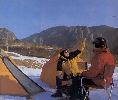 눈이 쌓인 야영장에서 기암을 바라보며 캠핑을 즐기는 캠퍼들.